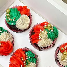 four cupcakes decorated with red, white and green frosting in a box