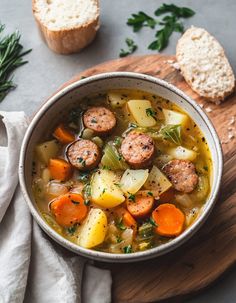 a bowl of soup with sausage, potatoes and carrots on a wooden cutting board