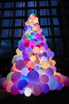 a large christmas tree made out of balloons in front of a building at night with the lights turned on