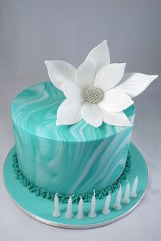 there is a blue cake with white flowers on the top and green icing around it