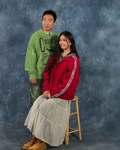 a man and woman posing for a photo in front of a blue backdrop with a wooden stool