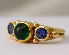 Exquisite 18k Royal yellow and rose gold hand fabricated ring, bezel set with a verdant Columbian emerald cabochon and matching slightly purplish blue Ceylon sapphires. The shank and bezels of the ring are made of recycled Royal yellow gold. Royal yellow is an 18k yellow gold European alloy which is much richer and less brassy than 18k American alloys. The ring is accented with 18k rose gold granules to give some extra dimension and depth.  The ring tapers from 8.5mm on the top to 3.1mm at the b Unique Gold Emerald Ring With Bezel Setting, Unique Yellow Gold Sapphire Ring With Bezel Setting, Unique Yellow Gold Emerald Ring With Bezel Setting, Unique Emerald Ring With Bezel Setting Gift, Green Sapphire Ring With Bezel Setting As Gift, Recycled Gold Ring, Royal Yellow, Emerald Cabochon, Columbian Emeralds