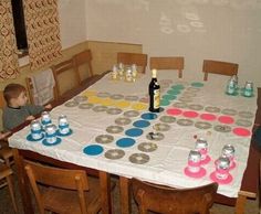 a child sitting at a table with cups and bottles on it, in front of a sign that says mogen die spiel beginen