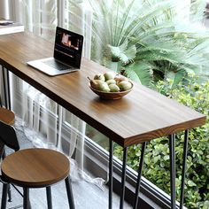 a wooden table with two stools and a laptop on it in front of a window