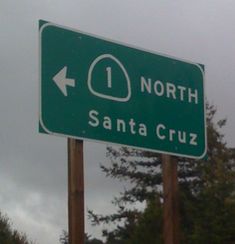 a green street sign with an arrow pointing to the north and santa cruz on it