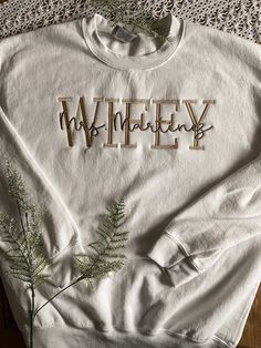 "PERSONALIZED WIFEY LAST NAME EMBROIDERED APPAREL ♡ Heavy Blend Crewneck Sweatshirt T - Unisex ♡ WIFEY - Custom Last Name Font ♡ 40/50 Cotton/Polyester ♡ Made in the U.S. ♡ ♡ Sample is \"White\"; Size: M, Font: \"Hayward\"; \"HUBBY\" Embroidery Thread: \"Tan\"; Last Name Embroidery Thread: \"Brown\" ADD A DATE TO THE SLEEVE: https://www.etsy.com/listing/1439827249/custom-date-with-rings-on-the-sleeve?click_key=c918760670f687f44ca2002e4fa85f35294390a3%3A1439827249&click_sum=a0de5211&ref=shop_home Last Name Embroidery, M Font, Embroidered Apparel, Wifey Sweatshirt, Mrs Sweatshirt, Letter Sweatshirt, Dog Mom Sweatshirt, Name Embroidery, Embroidered Crewneck