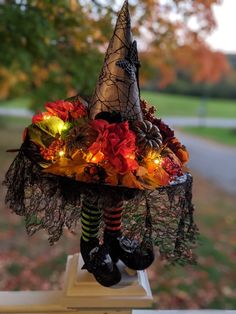 a witch's hat is decorated with lights and flowers on a white pedestal in front of a tree