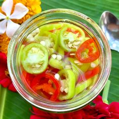 a glass jar filled with sliced vegetables on top of a green leafy table next to flowers