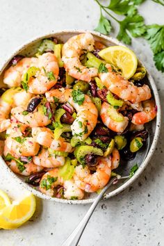 a bowl filled with shrimp and vegetables next to lemon wedges on a table top