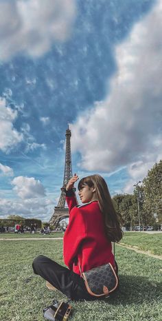 a woman sitting on the ground in front of the eiffel tower with her hand up