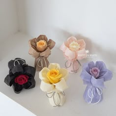 four different colored paper flowers on a white surface with string tied around the top and bottom