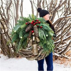 a woman carrying a wreath with bells and pine cones on her back in the snow