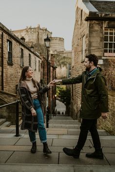 a man and woman are standing on the street pointing at each other's hand