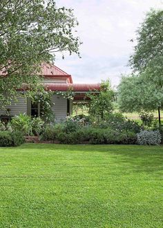 the house is surrounded by lush green grass and trees, with an old - fashioned red tin roof