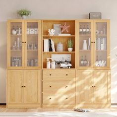 a wooden cabinet with glass doors and drawers in the middle of a white living room