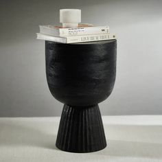 a black vase sitting on top of a table next to a stack of books in front of it