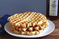 a stack of waffles on a white plate next to a bottle of syrup