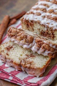 cinnamon roll bread with icing on a red and white checkered towel next to cinnamon sticks