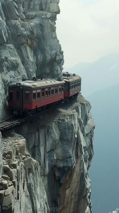 a red train is on the side of a rocky cliff with a mountain in the background