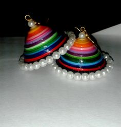 two multicolored bell shaped earrings with pearls hanging from each earring on a white surface