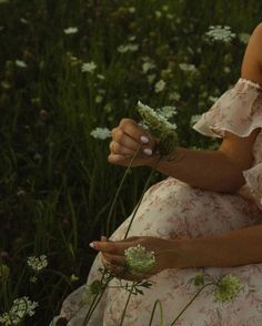 a woman is sitting in the grass with flowers on her hand and looking at the camera