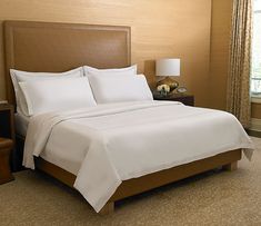 a bed with white sheets and pillows in a hotel room next to a lamp on a nightstand