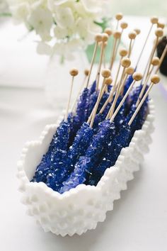 some blue and white toothpicks in a bowl on a table with flowers behind them