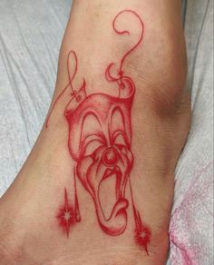 a tattoo on the foot of a person with an evil clown face and tongue sticking out