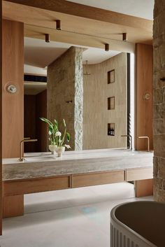 a bathroom with stone walls and a large mirror over the bathtub that has a potted plant in it