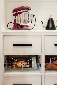 a kitchen with white cabinets and drawers filled with baking supplies, including an electric mixer