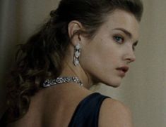 a woman in a black dress with large earrings on her neck looking off into the distance