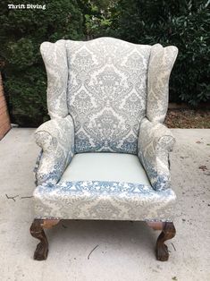 an upholstered chair with blue and white damask on the back is sitting in front of a brick wall