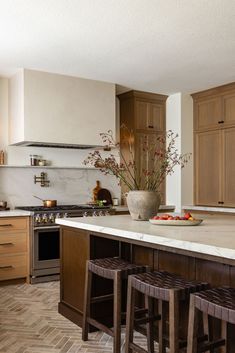 a kitchen with wooden cabinets and marble counter tops, two stools are in front of the island