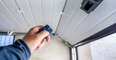 a hand holding a remote control in front of a ceiling fan and light on the wall