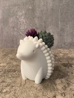 a white ceramic hedgehog planter with succulents on it's head