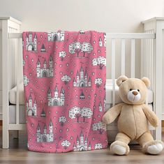 a teddy bear sitting next to a crib with a pink and white blanket on it