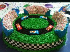 a birthday cake decorated with cars and sprinkles on top of green grass