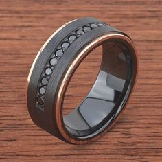 a wedding ring with black diamonds on it sitting on a wooden surface in front of a wood table