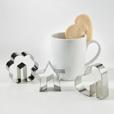 cookie cutters and cookies in the shape of hearts next to a coffee cup on a white background