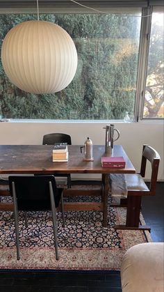 a wooden table with two chairs and a lamp hanging from the ceiling in front of a window