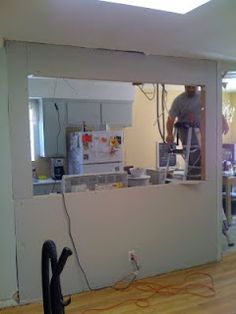 a man is working on the wall in his kitchen while another person stands behind him