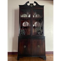 a wooden china cabinet with glass doors on the top and bottom shelves, in front of a white wall