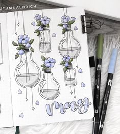 an open notebook with blue flowers in vases and writing on the page next to markers