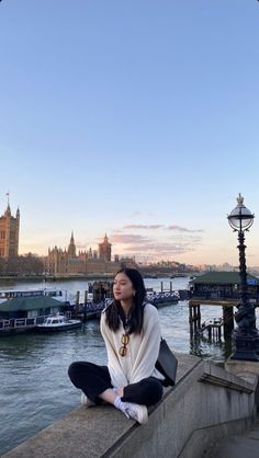 a woman sitting on the edge of a bridge looking up at the sky and buildings