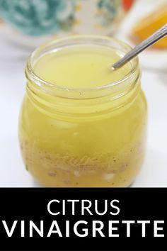 a jar filled with yellow liquid sitting on top of a white table next to a spoon