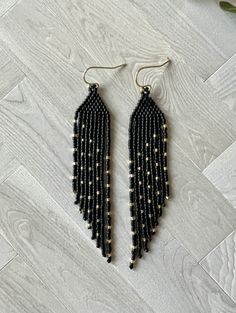 the black beaded fringe earrings are hanging from gold hooks on a white wood floor