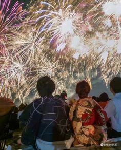 people watching fireworks in the night sky with their backs turned to the camera and looking at them