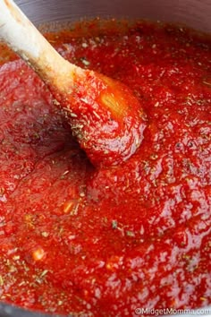 a wooden spoon stirring red sauce in a pot