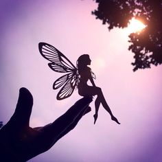 a hand holding a fairy figurine with the sun in the background