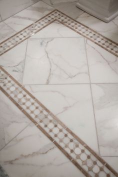 a bathroom floor with white and gold tiles on it's sides, including a toilet in the background